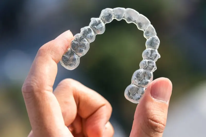 Hand holding a clear Invisalign aligner